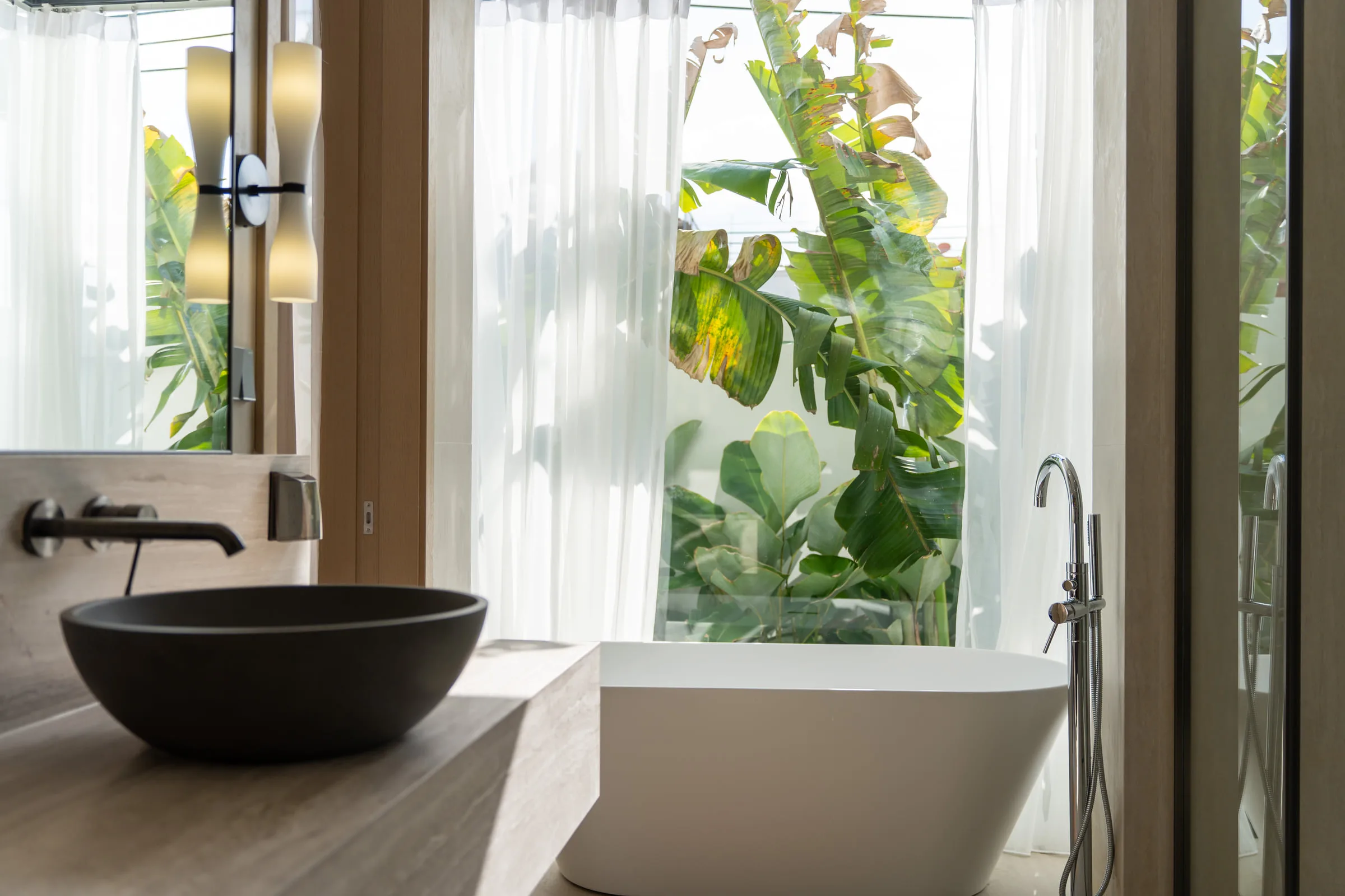 Bathroom with a freestanding bathtub and a stone basin, beside a window onto planting