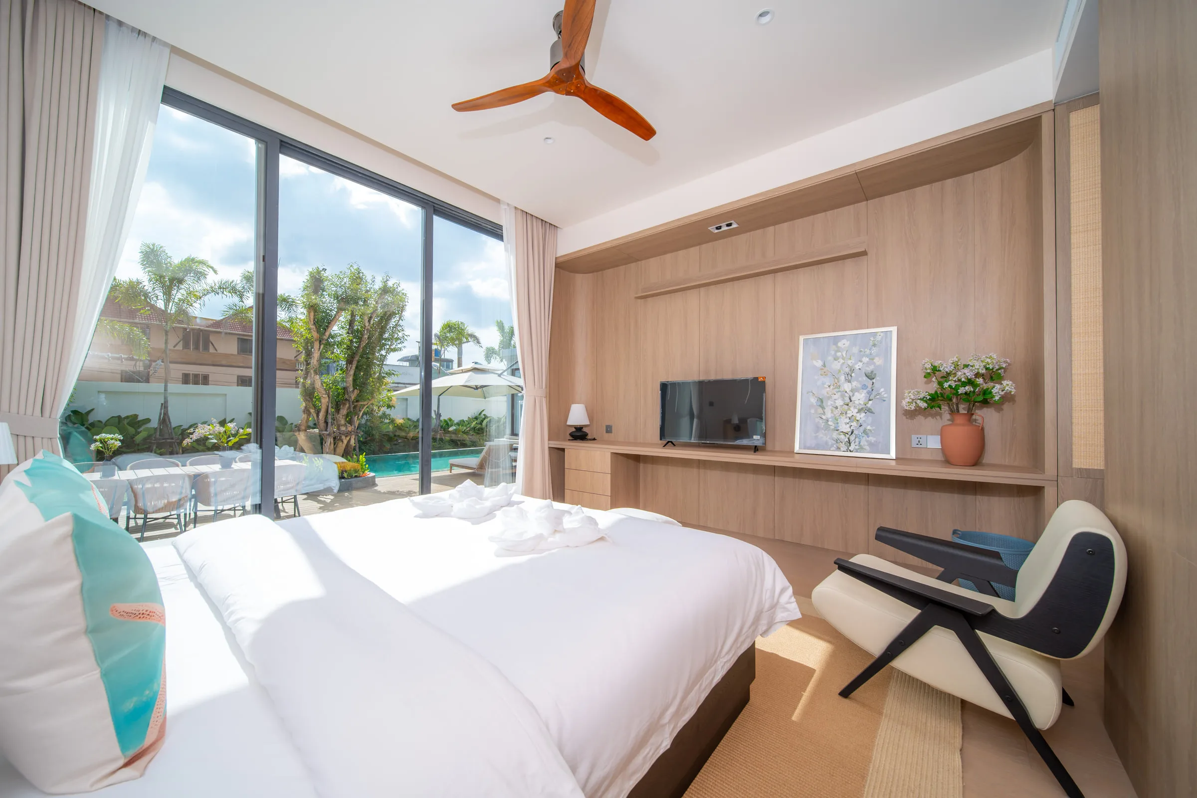 Bedroom with a double bed, wall-mounted television, desk and an armchair by the pool-facing window