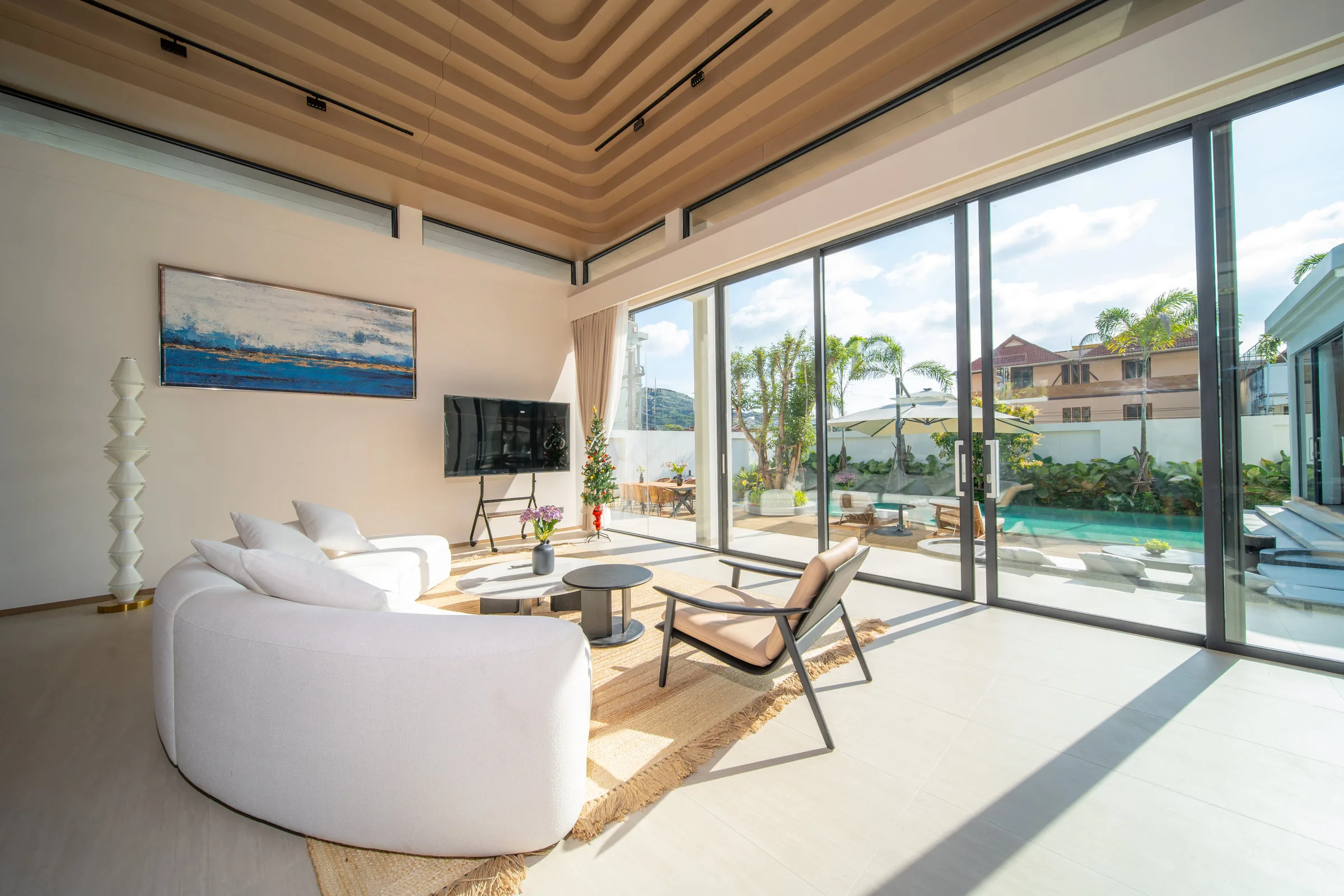 Living room with a curved sofa, armchairs and full-height glazing facing the pool