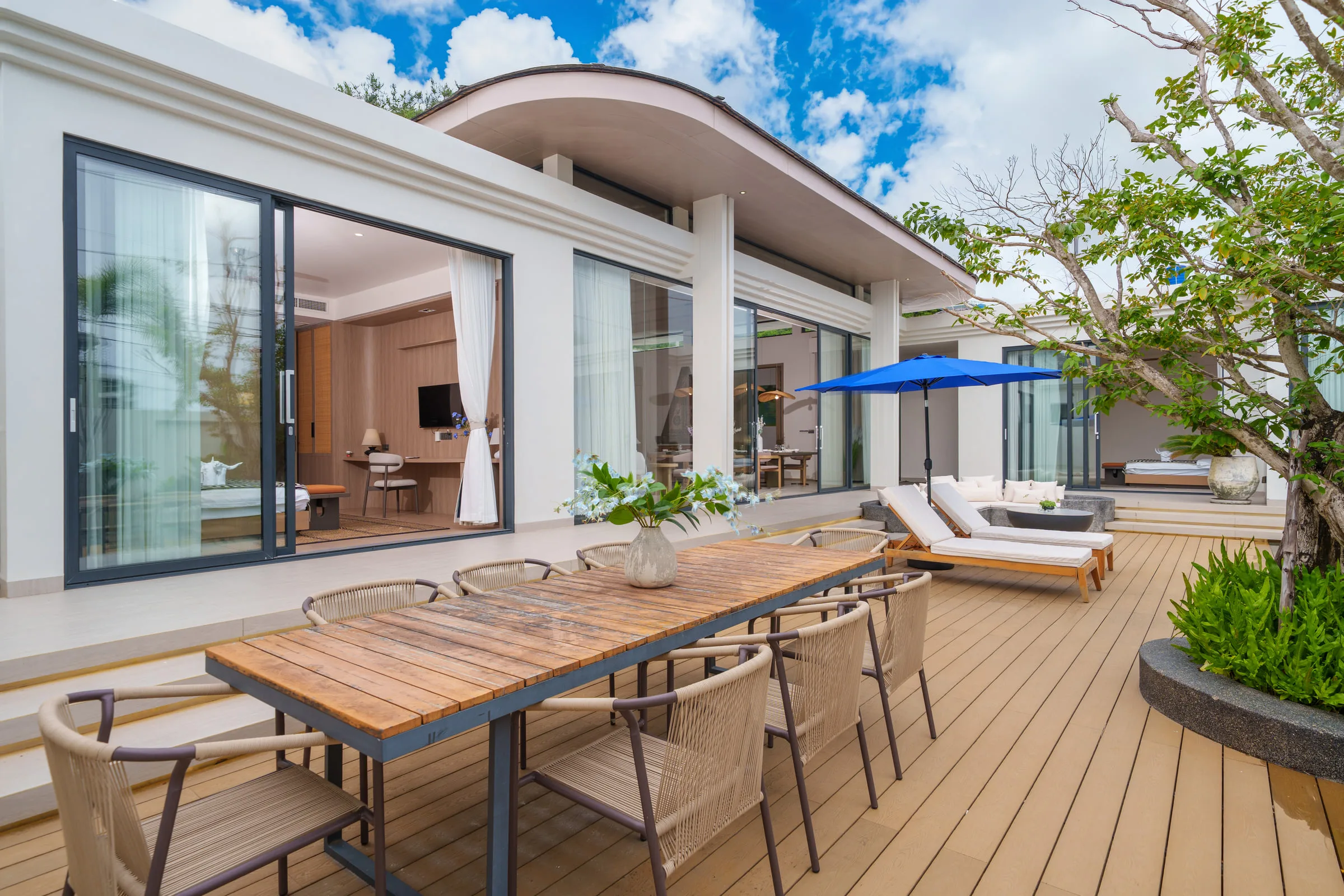 Villa exterior across the pool: single-storey wings, sliding glass doors and a timber pool deck