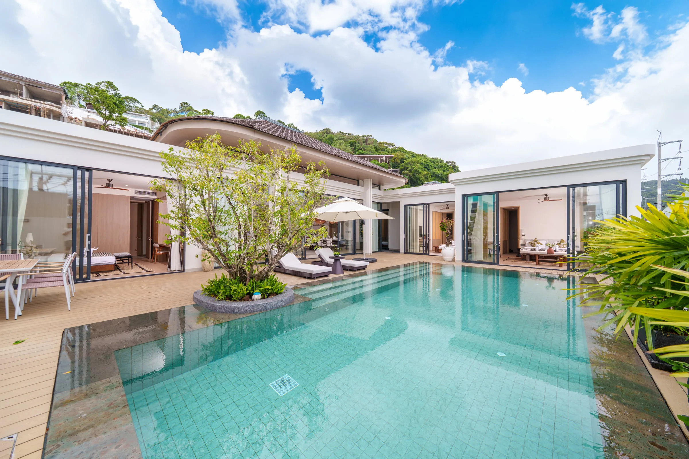Villa exterior across the pool, with the covered terrace open to the living room and a hillside behind