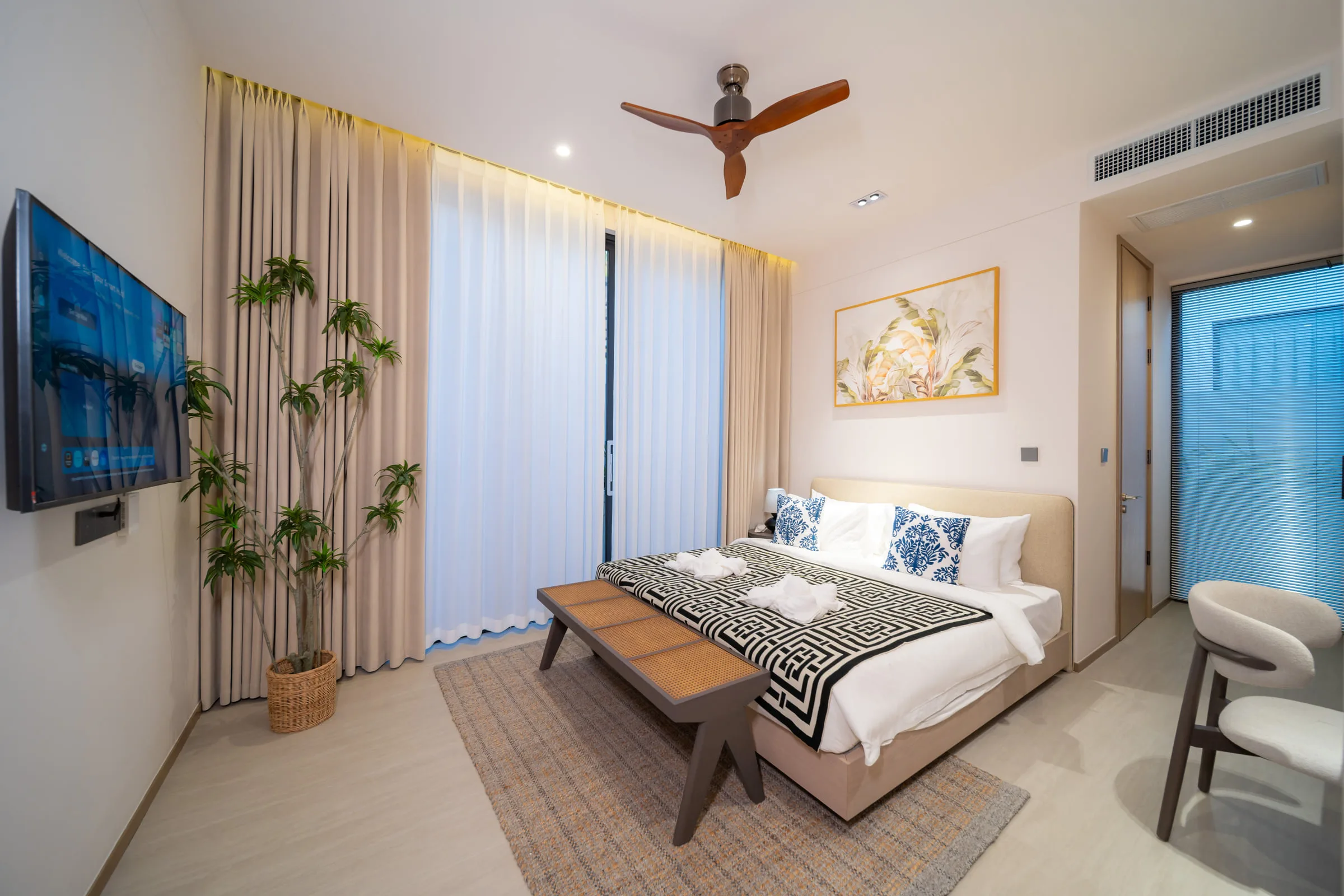 Bedroom with a wall-mounted television, curtained window and a bench at the foot of the bed