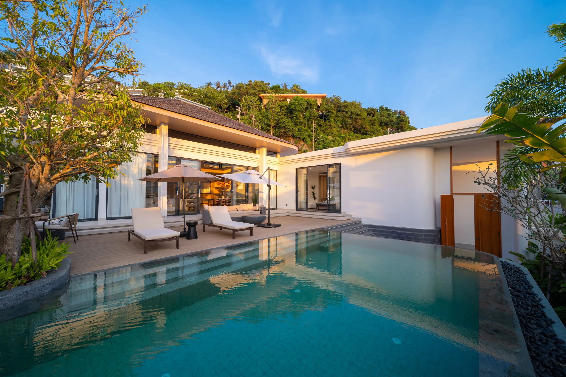Villa exterior across the pool in late afternoon light, with the hillside behind