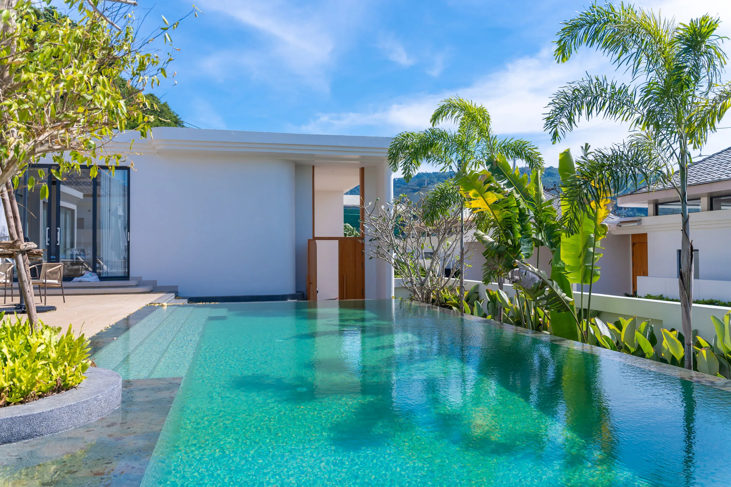 Swimming pool with palms along the boundary wall and the house on the left