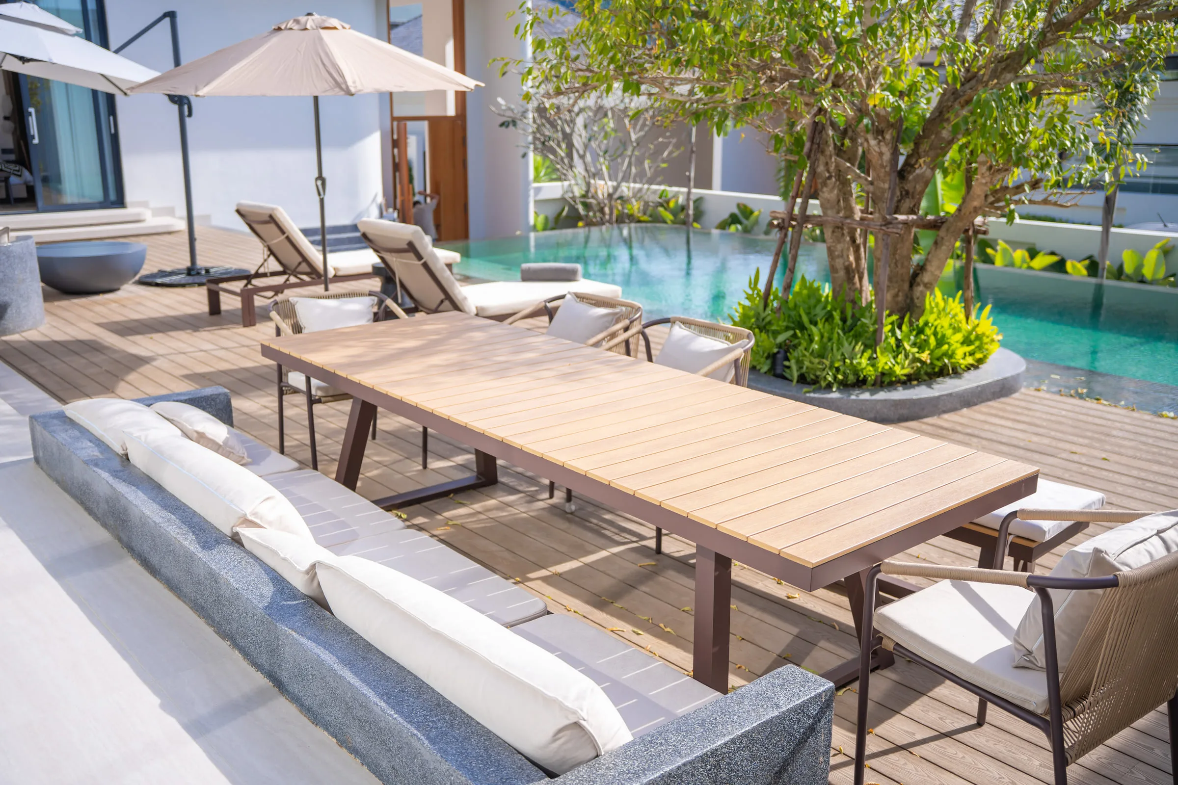 Covered terrace with an outdoor dining table, built-in seating and sun loungers by the pool
